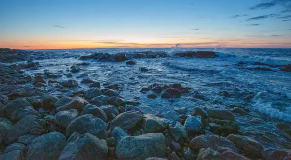 Stenstrand vid solnedgången. Vågor slår mot klipporna i det blåa vattnet. En lugn kväll, precis som det iso betyder.