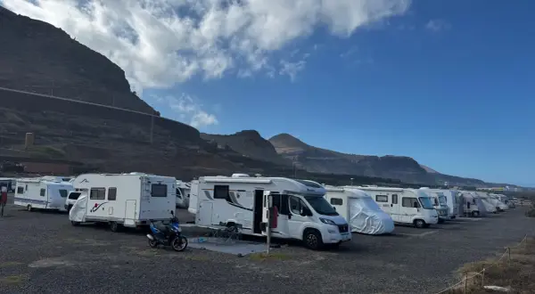 Un grupo de autocaravanas low cost aparcadas en un terreno pedregoso, con montañas y cielo azul de fondo.