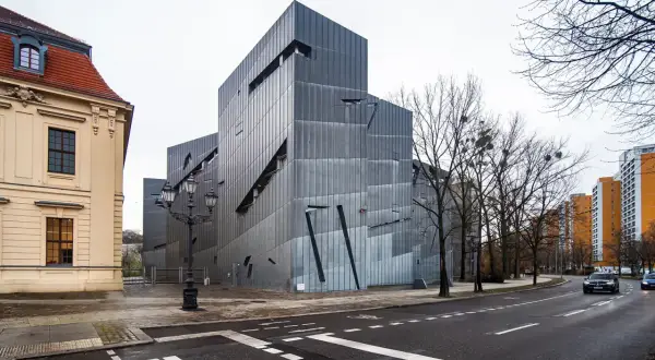Nowoczesny budynek muzeum żydowskiego w Berlinie, obok starszej kamienicy, z charakterystyczną, poszarpaną fasadą.