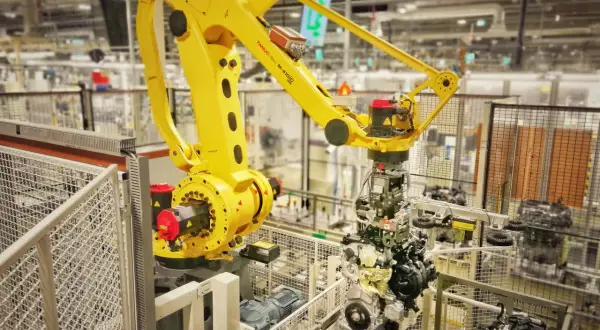 Żółty robot przemysłowy FANUC M-410iC pracuje nad montażem silnika, uosabiając filozofię kaizen toyota w nowoczesnej fabryce.