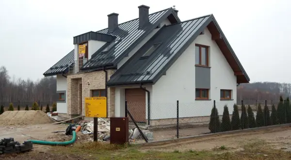 Nowy dom w budowie, widoczny przyłącze napowietrzne, plac budowy z piaskiem i materiałami.