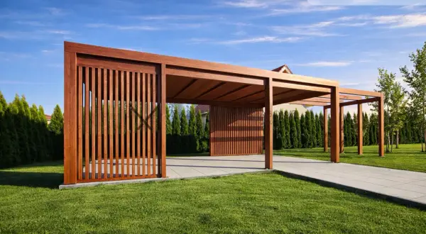 Drewniana pergola z pionowymi żaluzjami na tle zielonego trawnika i niebieskiego nieba.
