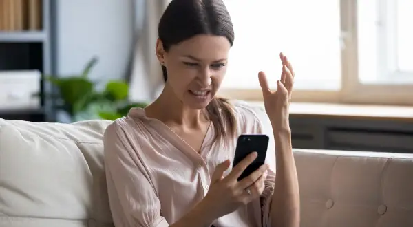 Femme frustrée sur son canapé, regardant son téléphone avec exaspération. Elle dit : "Je ne capte pas chez moi !