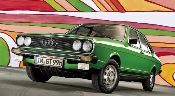 Grön Audi 50 står framför en färgglad, abstrakt bakgrund. Bilen har en klassisk design med kromdetaljer och en svart rand längs sidan.