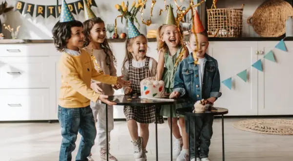 Radosne zabawy na urodziny 9 latki! Dzieci w czapkach urodzinowych śmieją się wokół tortu.