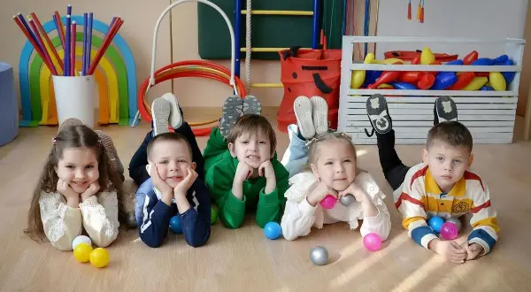Dzieci leżą na podłodze w żłobku, bawiąc się piłeczkami. To pokazuje, ile trwa adaptacja w żłobku.
