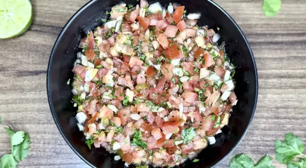Świeże, kolorowe pico de gallo w czarnej misce, z limonkami i kolendrą na drewnianym tle. Idealne do nachos!