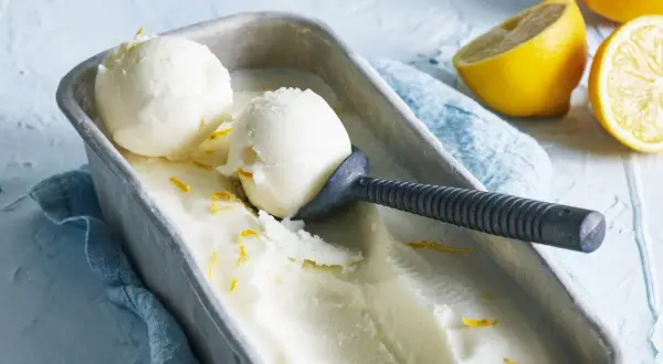 En metallform fylld med krämig italiensk citronsorbet, garnerad med citronskal. Två skopor är upptagna med en skopa.