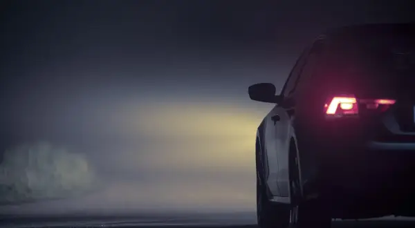 Vue arrière d'une voiture dans le brouillard, feux arrière allumés. L'emplacement des feux de voiture est bien visible.