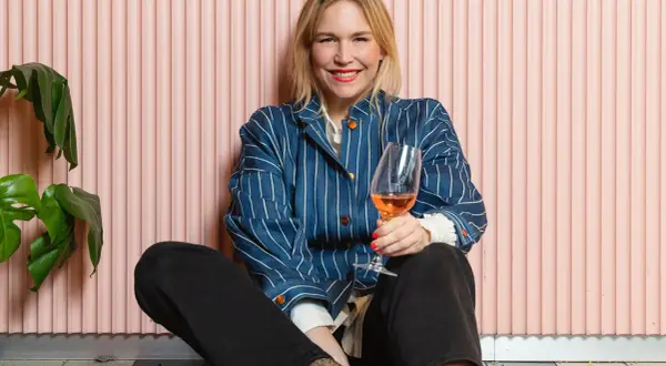 Frida Lund blogg: En glad kvinna med ett glas rosévin sitter på golvet framför en rosa vägg.