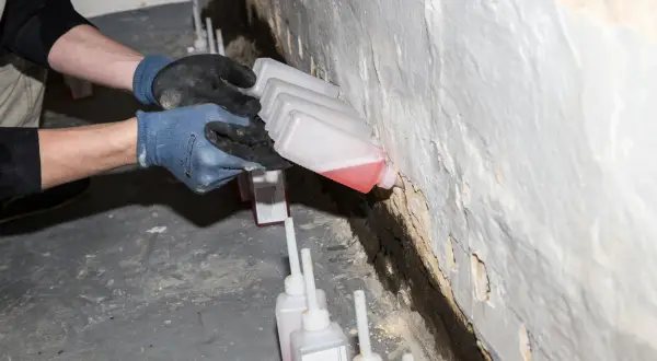 Hände mit Handschuhen führen kleine Flaschen mit roter Flüssigkeit an eine Wand, um Schachtringe abzudichten.