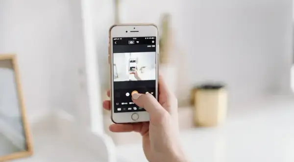 Dłoń trzyma smartfon, na ekranie którego widać aparat robiący zdjęcie. To jakby snapbridge po polsku, uchwycenie chwili.