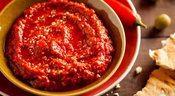 Pikantny sos adżika w miseczce, obok papryczek chili i oliwek. Idealny do pieczywa.