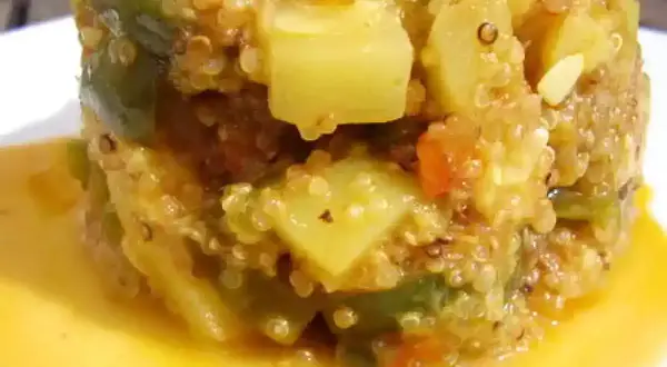 Un délicieux risotto de quinoa aux légumes verts et tomates, servi dans une sauce dorée.