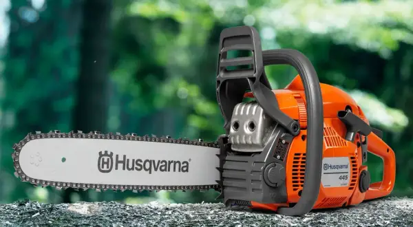 Pomarańczowa piła łańcuchowa Husqvarna 445 na pniu drzewa. Sprawdź husqvarna 445 dane techniczne, by poznać jej możliwości.