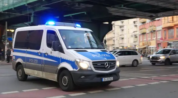 Polizeivan mit Blaulicht fährt auf der Straße. Ein polizeiliches Verkehrszeichen ist auf dem Fahrzeug angebracht.