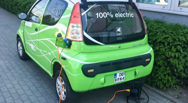 Zielony elektryczny samochód ROMET HE z napisem "100% electric" jest ładowany. To część programu "Mój Elektryk".