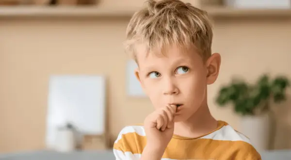 Chłopiec z blond włosami obgryza paznokcie, zastanawiając się, dlaczego dzieci to robią.