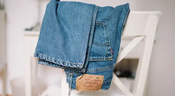 Złożone, klasyczne jeansy Levi Strauss wiszą na białym krześle. Widoczna metka z logo marki.