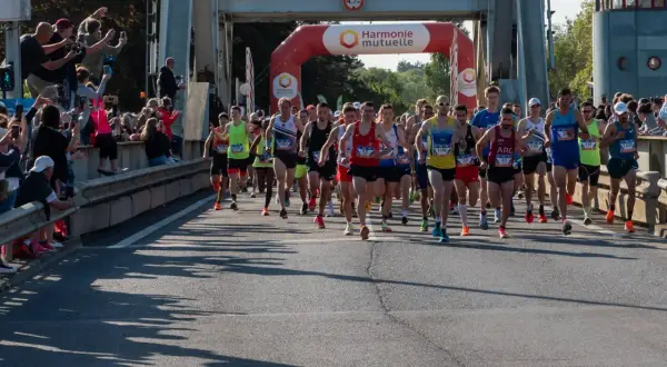 Coureurs au départ du semi-marathon Paris 2026, sous une arche Harmonie Mutuelle. Le soleil brille, les spectateurs encouragent.