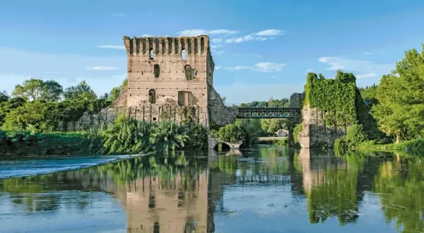 Rovine di un castello e un ponte sul Mincio, con riflessi sull'acqua calma.