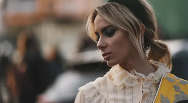Blonde Frau mit auffälligem Make-up und einem grünen Haarband, das ihre Frisur betont.