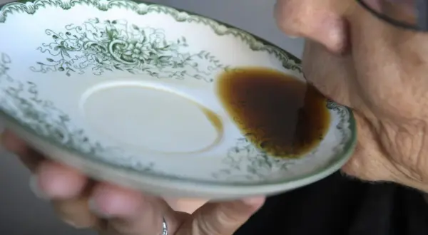 En person dricker gammalt kaffe direkt ur en tefat med grön dekor.