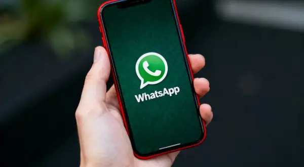 Dłoń trzyma iPhone'a z logo WhatsApp. Dowiedz się, jak przenieść czaty WhatsApp z Androida na iPhone.