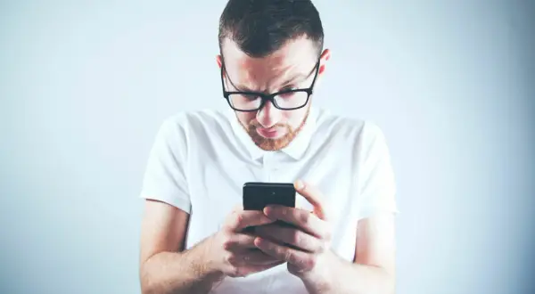 Zastanawiasz się, skąd firma windykacyjna ma Twój numer telefonu? Mężczyzna w okularach patrzy zdezorientowany na ekran smartfona.