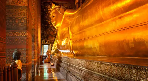 Stor gyllene liggande Buddha i ett tempel i Bangkok. En mindre Buddha-staty står till vänster.