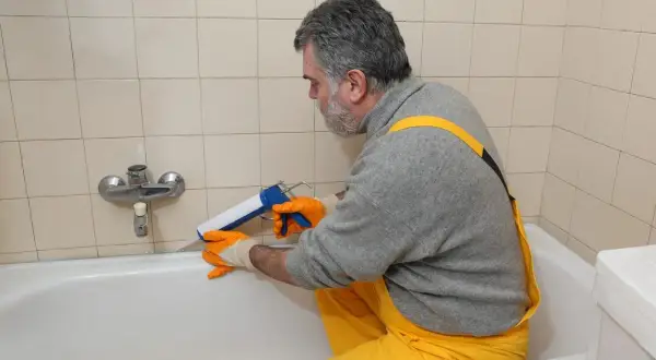 Mann erneuert mit Kartuschenpresse die silikonfugen an der Badewanne.