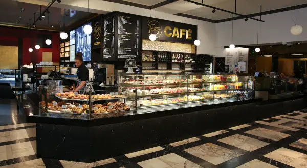En kvinna arbetar bakom disken på Fazer Café i Helsingfors. Disken är fylld med bakverk och tårtor.