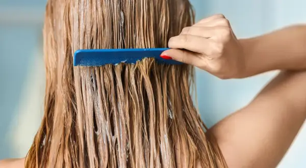 Une main peigne des cheveux blonds humides, recouverts d'un masque argile avant coloration végétale.