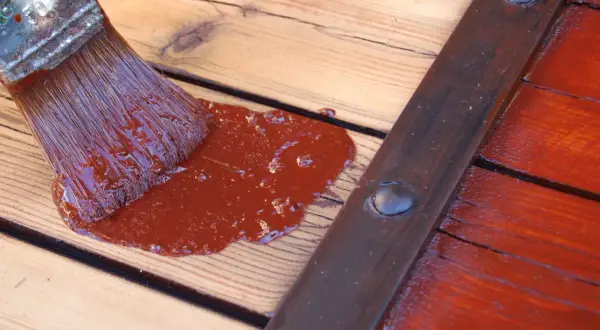 Pinceau appliquant une peinture marron sur des volets en bois sans décaper.