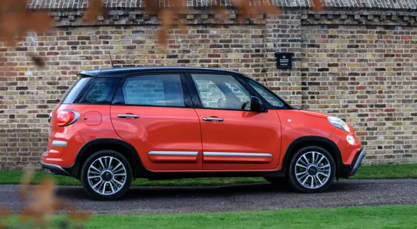 Pomarańczowy fiat 500xl z czarnym dachem stoi na tle ceglanej ściany.