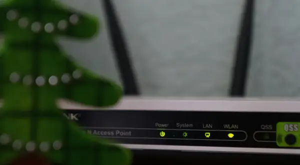 Świąteczna choinka obok routera, gotowa do konfiguracji sieci LAN. Wskaźniki Power, System, LAN, WLAN świecą się zielono.