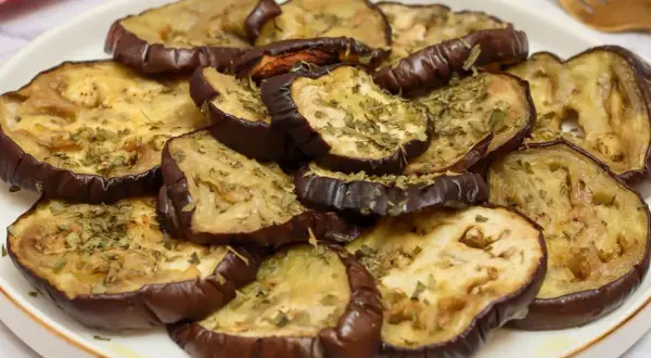 Rodajas de berenjenas asadas al horno, tiernas y doradas, espolvoreadas con hierbas aromáticas.