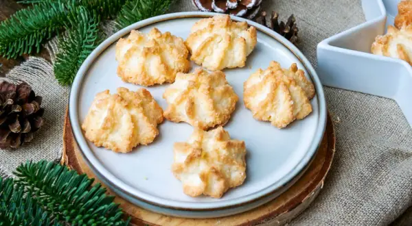 Leckere Kokosmakronen, die nach einem einfachen Rezept gelingen. Perfekt für die Weihnachtszeit, umgeben von Tannenzweigen und Zapfen.