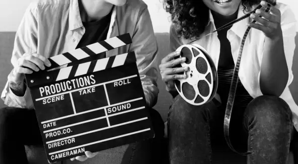 Dwie osoby z klapsem filmowym i rolką taśmy filmowej. Zastanawiasz się, ile zarabia producent filmowy?