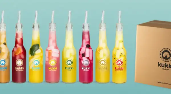 Reihe von Kukki Cocktails in Flaschen mit Früchten und Eis, daneben eine Pappbox.