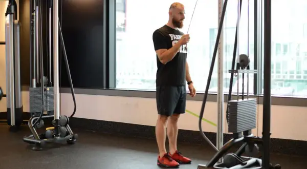 Mężczyzna wykonuje prostowanie ramion na wyciągu, ćwicząc triceps.