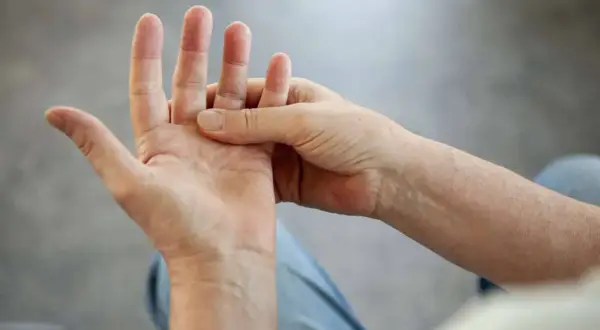 Person massiert Hand, da die Finger schmerzen beim Beugen.
