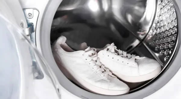 Weiße Sneaker warten im Inneren einer Waschmaschine auf ihren Einsatz.