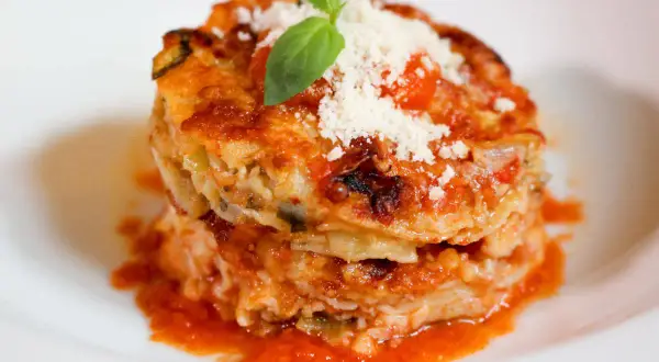 Parmigiana di alici, un tortino stratificato con pesce, verdure e pomodoro, guarnito con basilico e parmigiano.