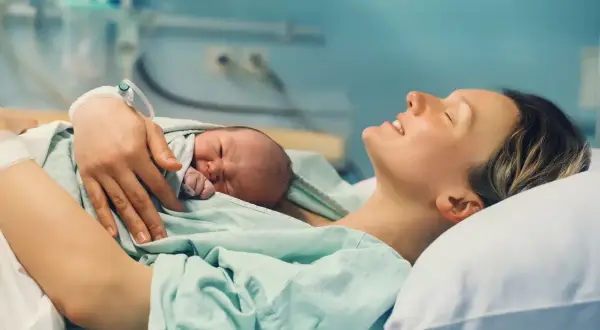Szczęśliwa mama tuli noworodka. To drugie dziecko, na które przysługuje 1000 zł.