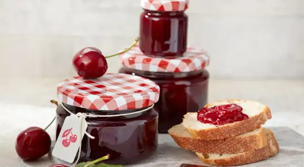 Gläser mit kirsch marmelade, frische Kirschen und Brot mit Marmelade.