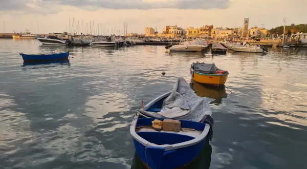 Barche nel porto al tramonto, con la città sullo sfondo. Un'atmosfera di pace e contemplazione, quasi un soffio di **santo spirito** sul mare calmo.