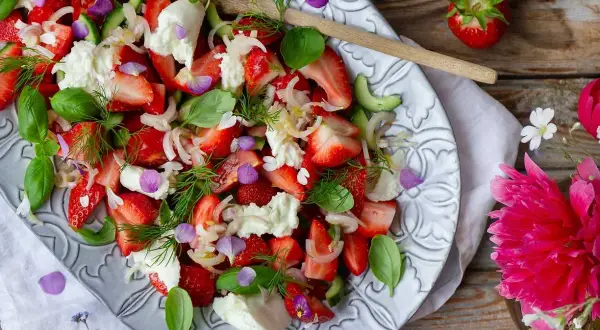 En härlig somrig sallad med jordgubbar, mozzarella, gurka och färska örter, dekorerad med ätbara blommor.
