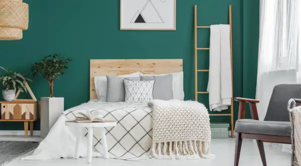 Chambre parentale cosy aux murs vert émeraude, lit en bois, plaids douillets et plantes vertes pour une ambiance relaxante.