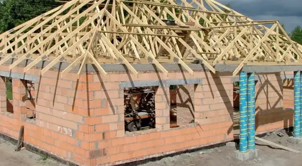 Budowa domu z cegły, na którym widać drewniany dach czterospadowy w konstrukcji.